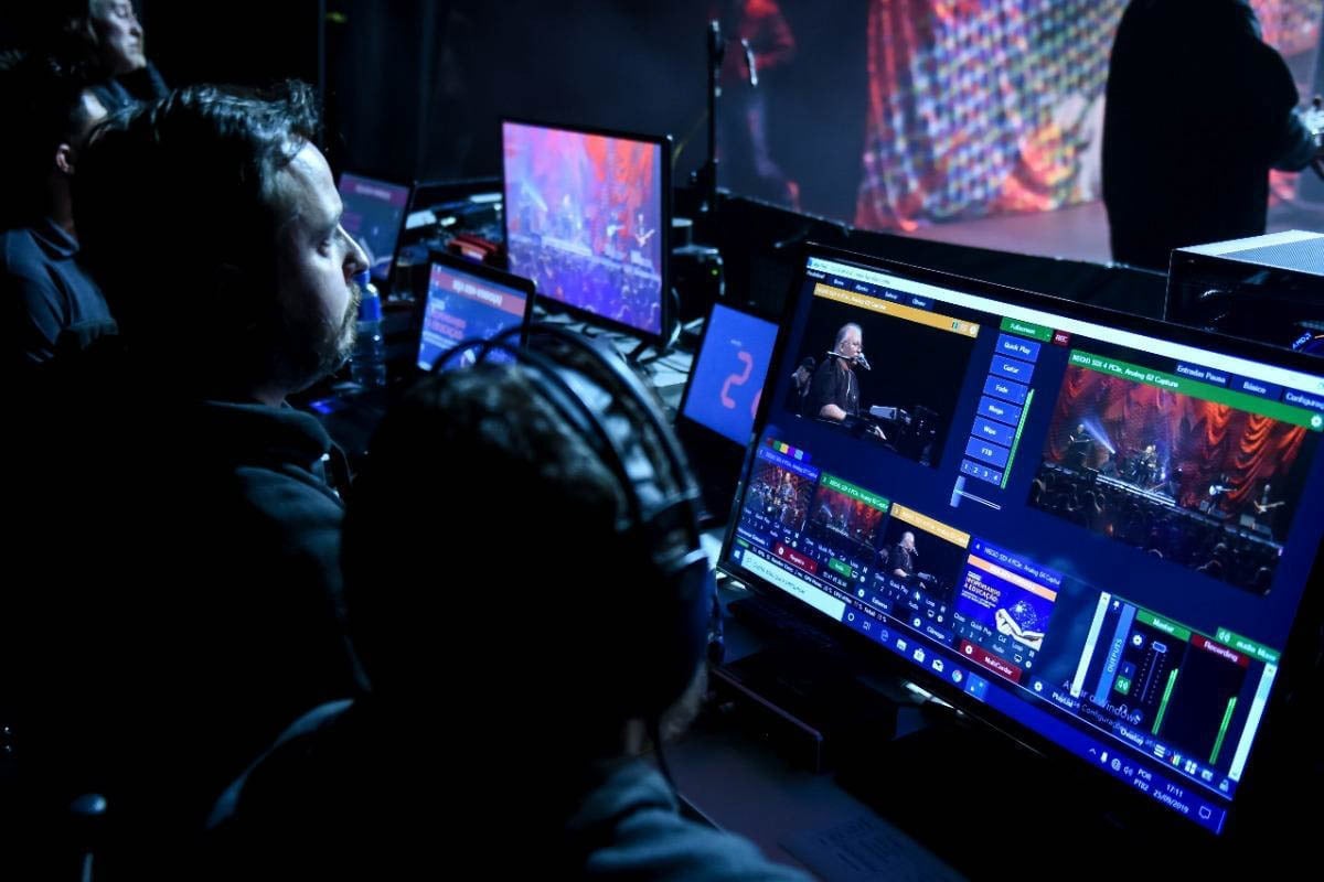 Live event production crew operating lighting and video mixing equipment during a performance with multiple displays and screens