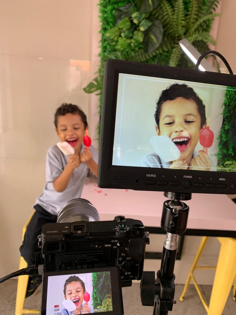 Child holding pink headphones laughing while recording on professional camera